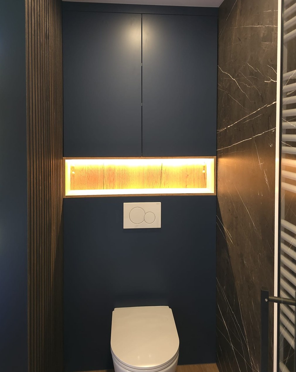 Hangtoilet tegen een blauwe kastenwand met verlichte nis en houten lamellen