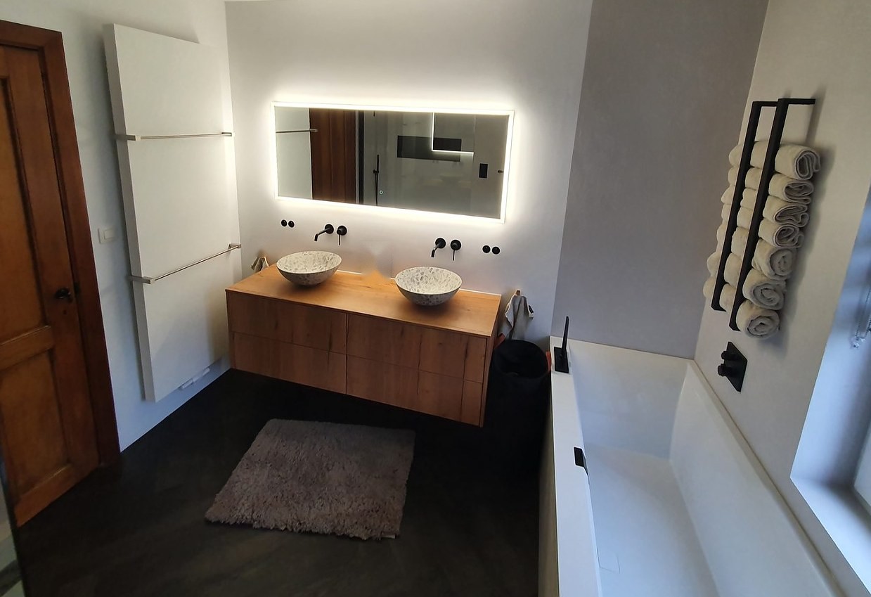 Badkamer met eikenhouten dubbel meubel, verlichte spiegel, inbouwbad en zwart handdoekrek