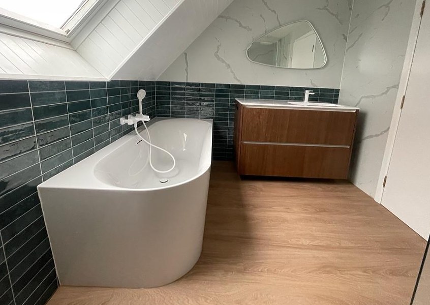 Zolderbadkamer met hoekbad, groene metrotegels, wit marmerlook en houten meubel
