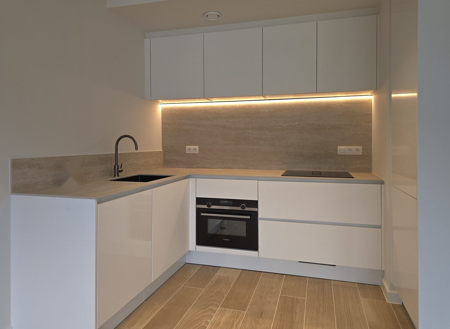 Witte hoekkeuken met verlichte achterwand, inbouwoven en houten vloer