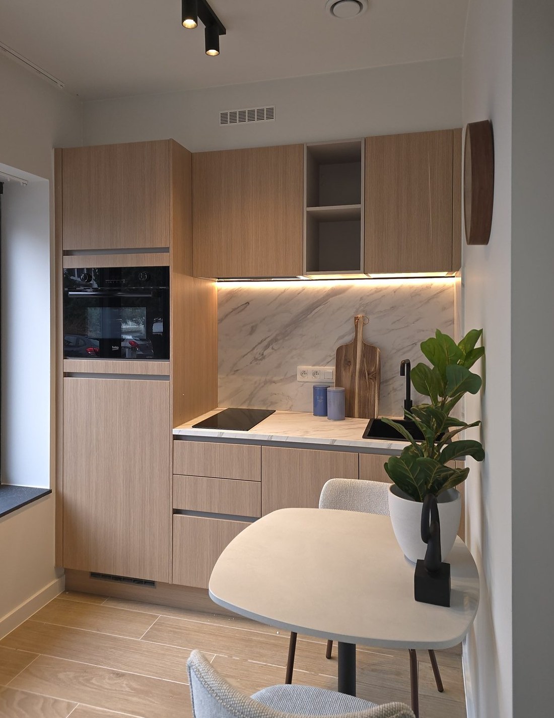 Compacte keuken in licht hout met marmerlook achterwand en klein eettafeltje