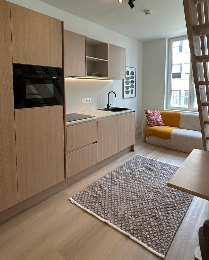 Studiokeuken in licht eikendecor met hoge kast, inbouwoven en zithoek