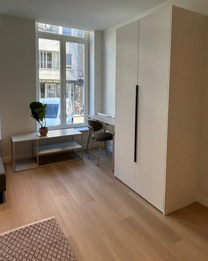 Studio met witte maatkast tot aan het plafond en bureauhoek bij het raam